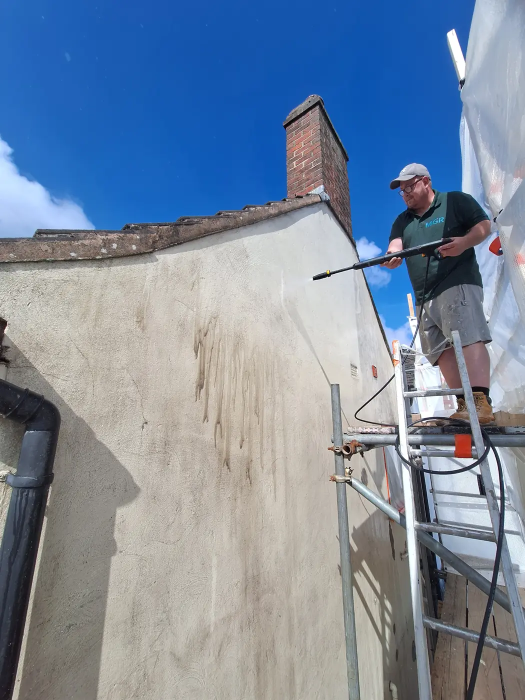 Team member pressure-washing a stained gable wall before coating
