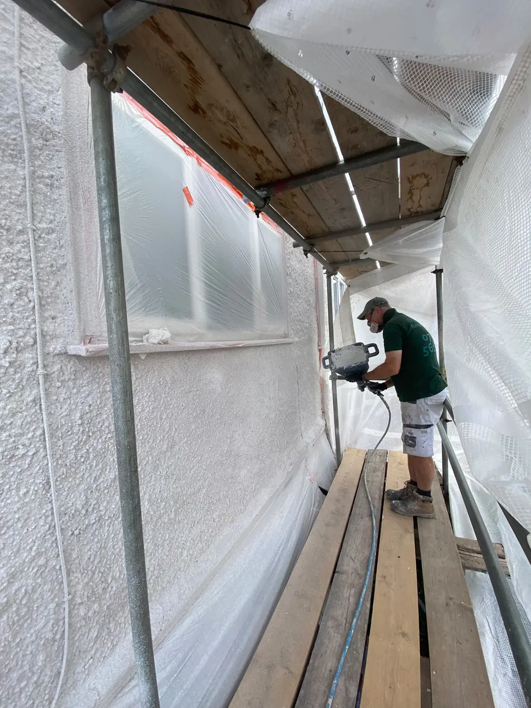 Applicator spraying CorkSol cork coating on a scaffolded wall
